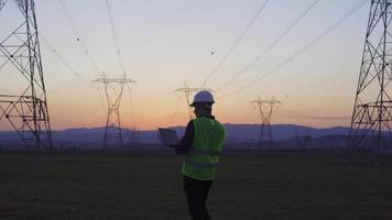 Engineer walking between electrical towers. Engineer with laptop in hand walks between power poles and inspects. He takes notes on the laptop and looks at the poles. video