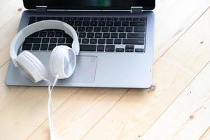 auriculares blancos y ordenador portátil sobre fondo de madera foto