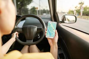 mujer en el auto y sosteniendo un teléfono móvil con mapa de navegación gps