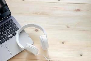 auriculares blancos y ordenador portátil sobre fondo de madera foto