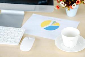 Business and workplace concept. Cup of hot coffee on work desk with computer keyboard and papers graphs photo