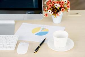 Business and workplace concept. Cup of hot coffee on work desk with computer keyboard and papers graphs photo