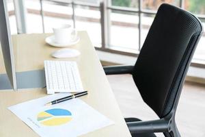 concepto de negocio y lugar de trabajo. taza de café caliente en el escritorio con teclado de computadora y gráficos de papeles en la sala de trabajo de la oficina. foto