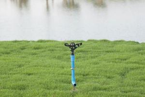 Ready-to-install watering sprinkler on green lawns on the quiet countryside lakeside, developing into a relaxing shelter. photo