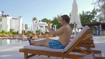 uomo che beve un cocktail a bordo piscina. sorseggiando un drink a bordo piscina. relax in piscina. video