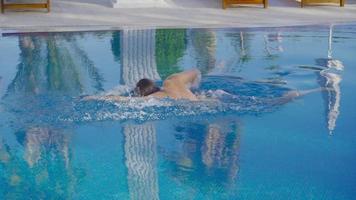 o homem nadando na piscina. jovem nadando na piscina. palmeiras refletidas. video