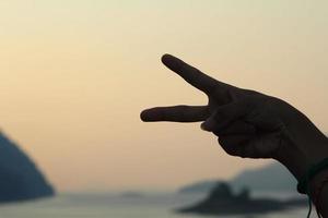 Two-finger symbol, index finger and middle finger, symbol of peace on the background Mountains, rivers and blue skies Attractive nature photo