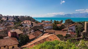 panorama del antiguo distrito de kaleici en antalya con un gran número de casas de piedra, palmeras, un terraplén, en las montañas de fondo foto