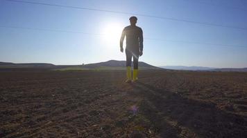 granjero caminando en el campo. camina con botas amarillas en una tierra de cultivo. mira a su alrededor y examina el terreno.