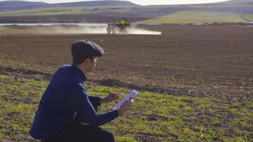 tracteur agrochimique et agriculteur moderne. la pulvérisation se fait avec un tracteur sur le sol des terres agricoles. un agriculteur travaille avec une tablette à la main. video