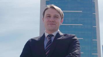 Luxury buildings and businessman. Businessman looking at camera in front of luxury buildings folds his arms and smiles.  Modern businessman in suit. video