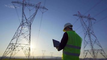 ingeniero eléctrico haciendo un estudio del sitio. ingeniero revisando postes de energía en el campo y trabajando en una computadora portátil. video