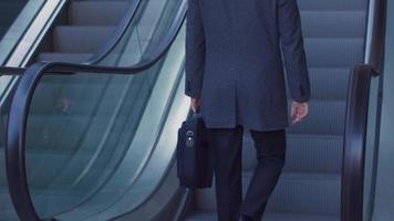 Businessman with bag going up the escalator. Businessman with briefcase in front of a luxury business building goes up the escalator. Image of modern building and modern businessman. video