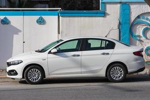 Side  Turkey  February 18 2022 white Fiat Egea   is parking  on the street on a  summer day against the backdrop of a   hotel, fence photo