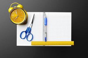 illustration, an open checkered notebook, a blue pen, scissors and an alarm clock on a black table are ready for the lesson. Stationery.Back to school photo