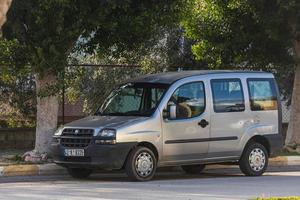 Side  Turkey  February  20, 2022  silver Fiat Doblo   is parked  on the street on a warm summer day against the  road and trees photo