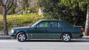 Side  Turkey  February 18 2022 black   Mercedes-Benz E-class is parked  on the street on a warm  day against the backdrop of a park, trees photo