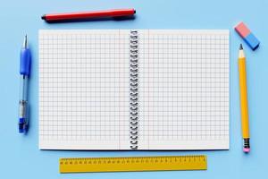 illustration, an open checkered notebook, a blue pen,  pencil, rubber, ruller and marker  on a blue table are ready for the lesson. Stationery.Back to school photo