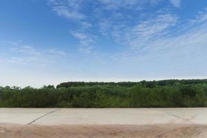 Horizontal view of concrete road in Thailand. Ground in front of dirt roads and floating tires. Background of green grass. and Young seedlings of cassava fields and rubber trees. Under the blue sky. photo