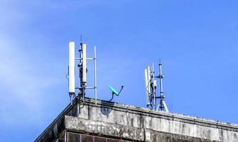 dispositivos y receptores de señal de comunicación con antenas en la parte superior del edificio y fondo de cielo azul brillante. foto