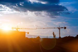 Silhouette of the hoisting cranes working building construction under the bright blue sky and big cloud in the evening with lens flare. photo