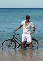 Young man standing in the ocean with his bicycle and his arms raised photo