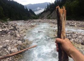 Point of view of a hiker with hiking stick in front of a small mountain river photo