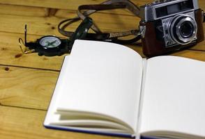 un diario de viaje vacío con una cámara y una brújula anticuadas foto