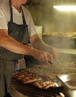 hombre vestido con un delantal trabajando en la parrilla de barbacoa foto