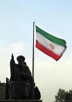 Tehran, Iran - June 10, 2018 - A large Iranian flag waving in the wind behind a statue of Khomeini in Tehran, Iran photo