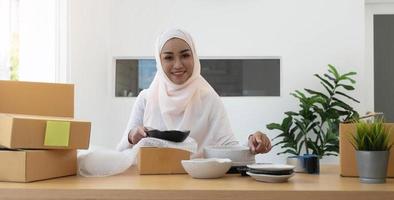 mujer musulmana propietaria de un negocio que trabaja en compras en línea prepara el proceso de empaque del producto en la oficina, concepto de joven emprendedor. foto