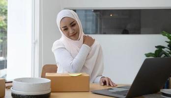 A portrait of a cute smiling teenage Muslim woman wearing a light pink hijab sits in a chair and closes her eyes to take a few naps after exhausting her hard work. overtime concept photo
