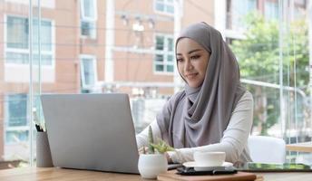 mujer de negocios musulmana asiática con velo hijab trabajando con computadora portátil en la oficina moderna. gente de negocios, diversidad y concepto de oficina foto