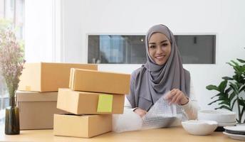 mujer musulmana propietaria de un negocio que trabaja en compras en línea prepara el proceso de empaque del producto en la oficina, concepto de joven emprendedor. foto