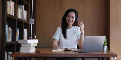 una mujer asiática que usa auriculares estudia en línea viendo un podcast de seminario web en una computadora portátil escuchando un curso de educación de aprendizaje conferencias telefónicas, concepto de aprendizaje electrónico. foto