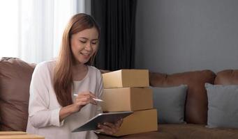Young asian woman is entrepreneur work from home with online on laptop, online shopping, logistic and delivery, female is seller working on sofa, business SME photo