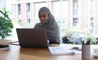 Young asian muslim business woman in smart casual wear discussing business and smiling while sitting in the creative coworking. photo