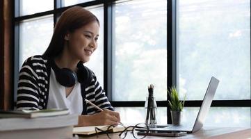 una joven estudiante asiática inteligente que aprende idiomas durante los cursos en línea de Internet y busca información a través de una computadora portátil en casa foto