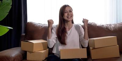 Happy young Asian woman entrepreneur, Smile for sales success after checking order from online shopping store at home office, Concept of merchant business online and eCommerce photo