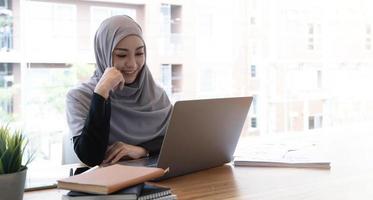 Happy beautiful muslim business woman brown hijab working about financial with business report and calculator in home office. photo