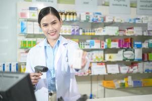 Farmacéutica femenina escaneando código de barras en una caja de medicamentos en una farmacia moderna. foto