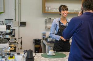 Young service minded barista woman with customer in coffee shop photo