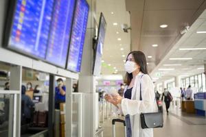 A traveller woman is wearing protective mask in International airport, travel under Covid-19 pandemic, safety travels, social distancing protocol, New normal travel concept . photo