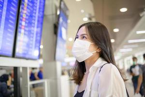 A traveller woman is wearing protective mask in International airport, travel under Covid-19 pandemic, safety travels, social distancing protocol, New normal travel concept . photo