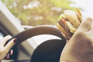 señora conduciendo un coche mientras come una hamburguesa foto