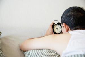hombre soñoliento sosteniendo el despertador por la mañana con despertar tardío - concepto de vida diaria en casa foto