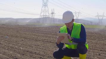 ingeniero trabajando con tableta y examinando el suelo. el ingeniero que trabaja en el campo con una tableta toma el suelo en su mano y lo examina. toma notas en la tableta. agricultura moderna. video