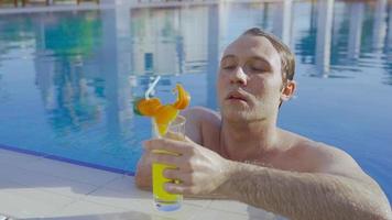 hombre feliz bebiendo jugo de naranja junto a la piscina. bebiendo jugo en la piscina