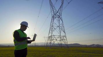 engenheiro trabalhando na frente de postes elétricos. engenheiro trabalhando no laptop na frente de postes elétricos. realizando pesquisas de campo. engenheiro elétrico. video