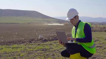 tracteur agrochimiste et ingénieur. la pulvérisation agricole est effectuée par le tracteur sur le sol des terres agricoles. un ingénieur travaille sur l'ordinateur portable dans sa main. video